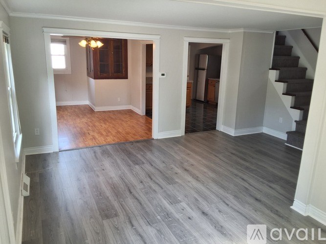A spacious room with wood flooring and a staircase.