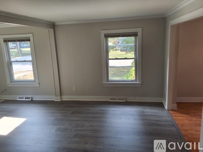 A room with two windows and wooden floors is available for rent.