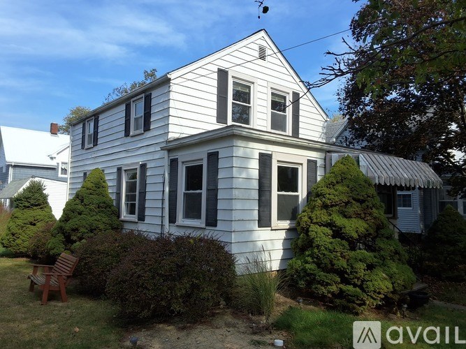 A white house with a grey roof and a brown bench in front of it.
