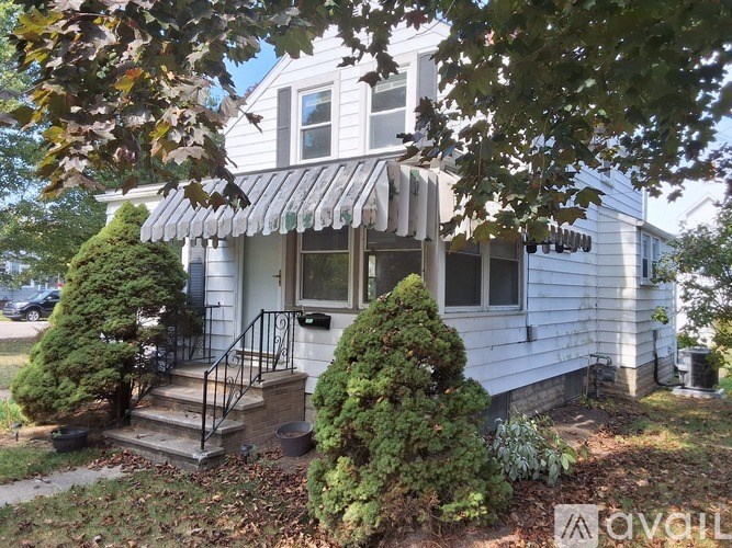 A white house with a porch and a tree in front.