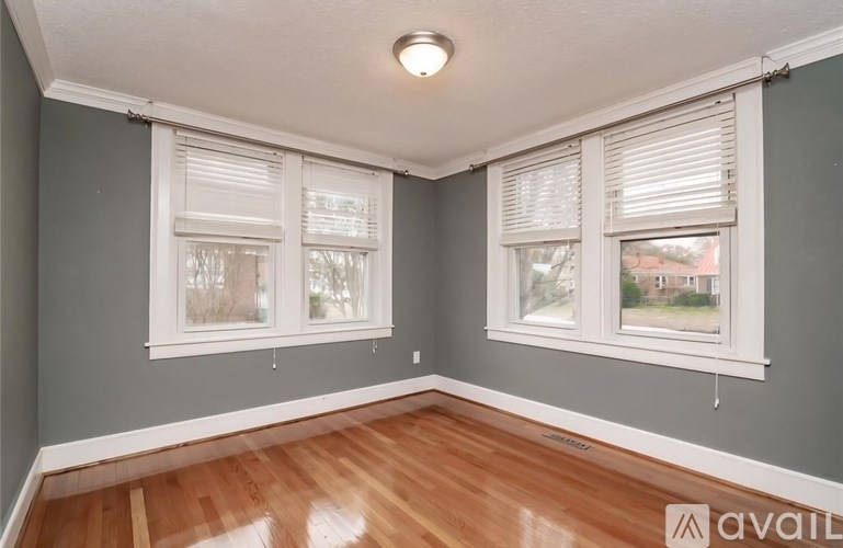 A room with wooden floors and two windows with white blinds.