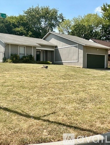 A house with a green garage door and a brown dog on the lawn.