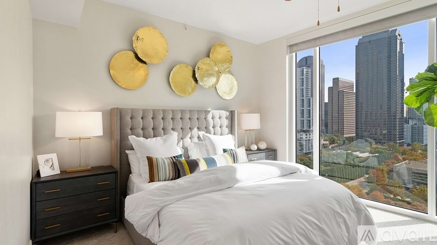 A bedroom with a large bed, a nightstand with a lamp, and a view of the city.