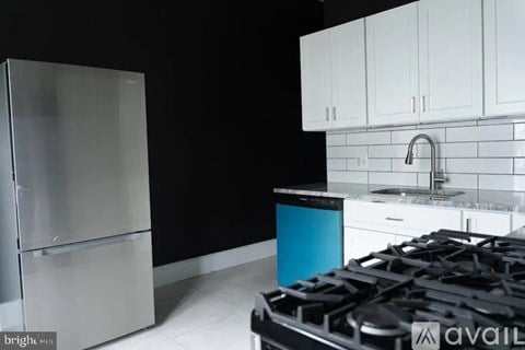 A modern kitchen with a stainless steel refrigerator, white cabinets, and a black gas stove.