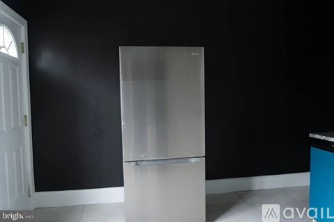 A tall, empty, white fridge stands in a room with black walls.