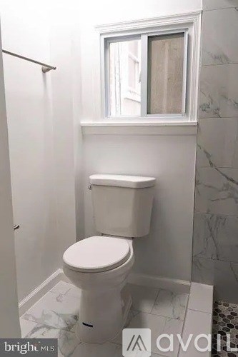 A white toilet in a bathroom with a window above it.