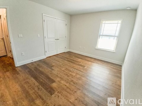 A room with wooden flooring and a window with blinds.