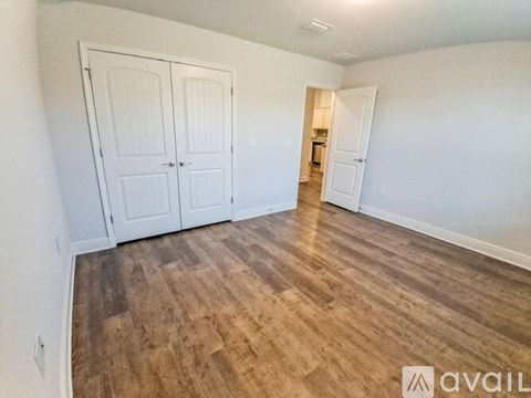 A room with wooden flooring and white walls, featuring a set of double doors and a smaller doorway.