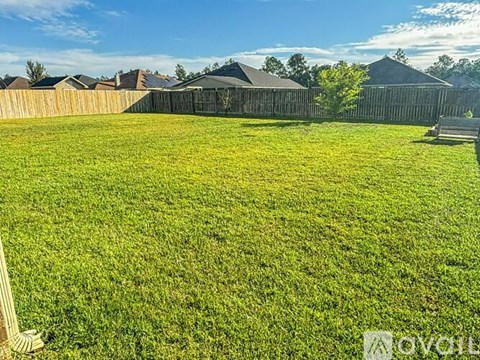 A grassy field with a fence and houses in the background.