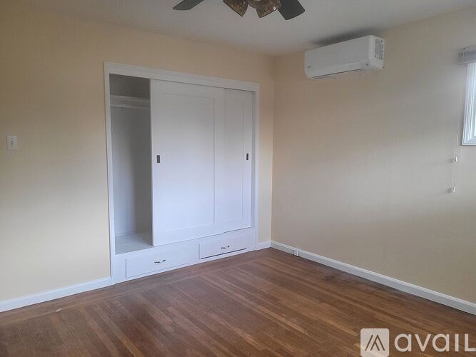 A room with a wooden floor, a white door with a mirror, and a ceiling fan.