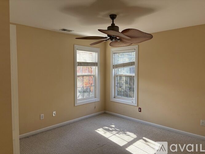 A room with a ceiling fan and two windows.