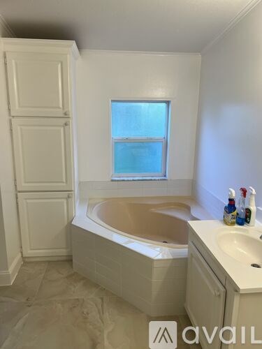 A white bathroom with a tub, sink, and window.