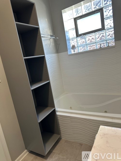 A bathroom with a tub, a window, and a shelving unit.