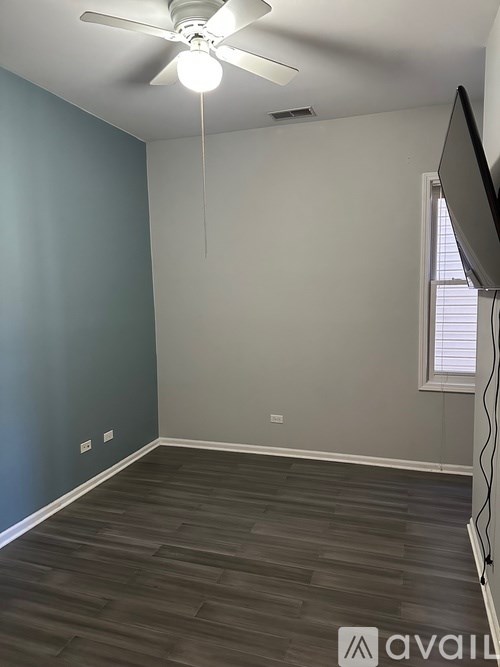 A room with a ceiling fan and a flat screen TV mounted on the wall.