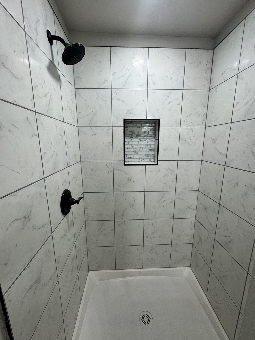 A white tiled bathroom with a shower head and a drain.