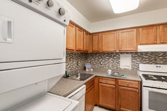 Kitchen with maple cabinets, white appliances, tile backsplash. and in-unit stacked laundry