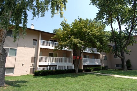 A tree in front of a building with a balcony.