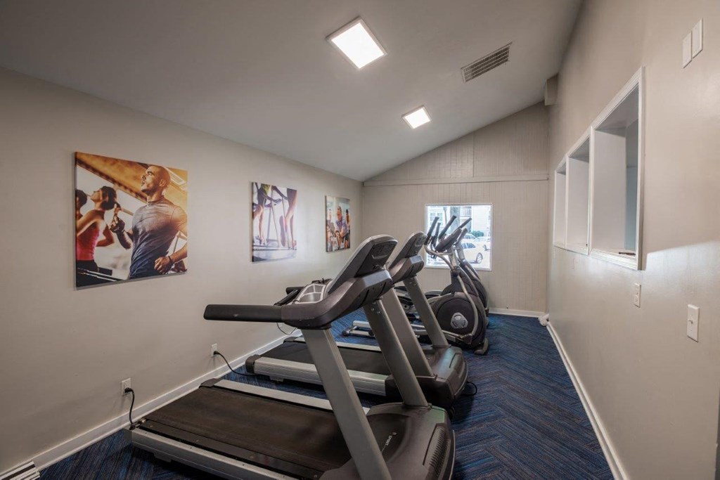 A treadmill is in a room with a wall art of people.