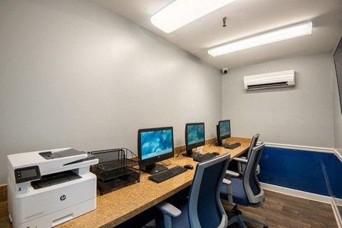 a room with a desk with three computer monitors and a printer