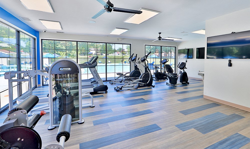a gym with cardio equipment and windows with a view of a pool