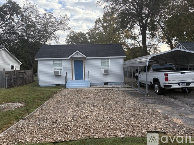 A small white house with a blue door and a gravel driveway.