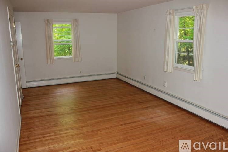 A room with wooden flooring and two windows with curtains.