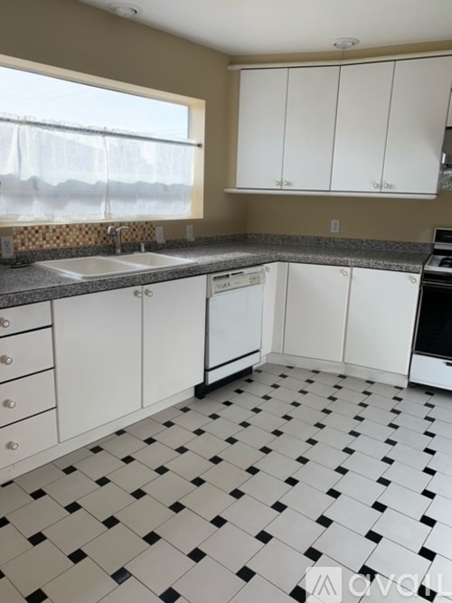 A kitchen with white cabinets and black and white checkered floor.