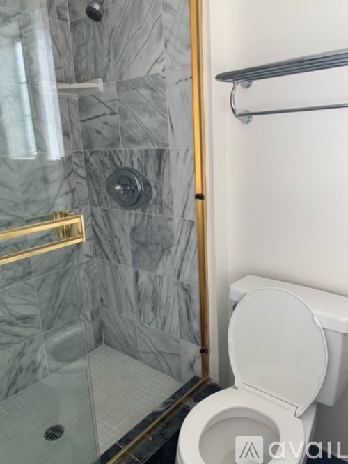 A toilet in a bathroom with marble tiles and a gold-framed shower.