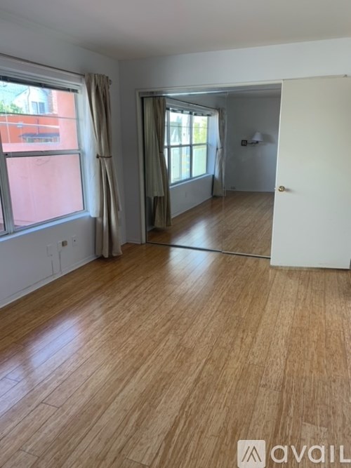 A room with wooden flooring and a large window with curtains.