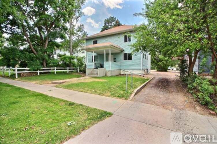 A house with a green fence and trees in front.