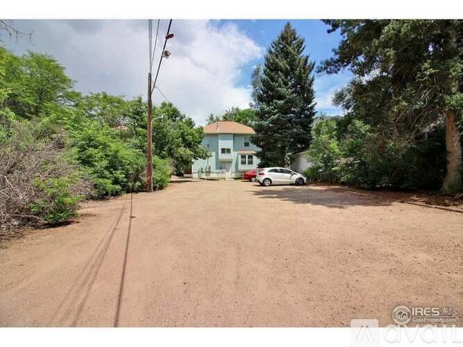 A dirt road leads to a house with a car parked in front.