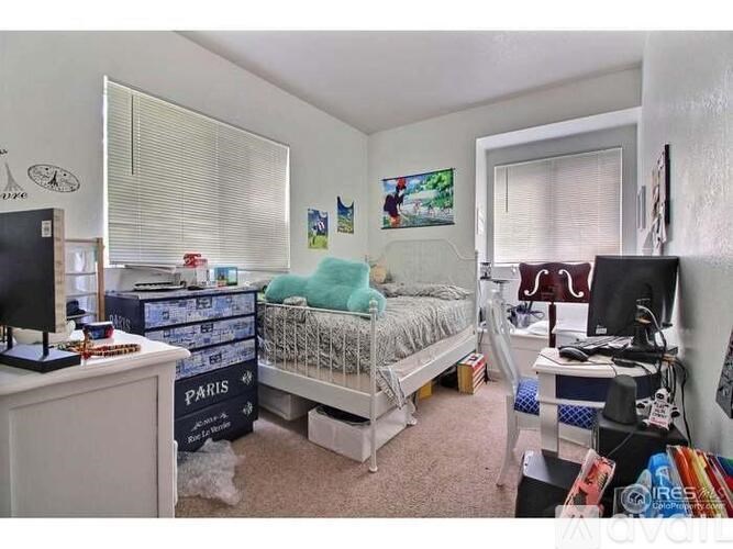 A bedroom with a bed, desk, and a window with blinds.