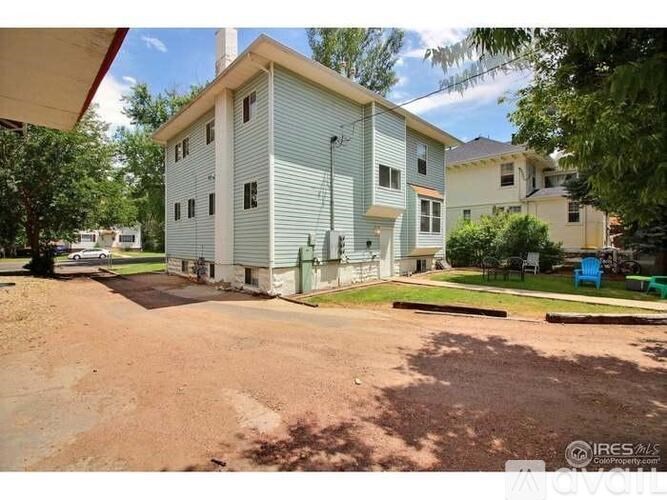A two-story building with a blue and white exterior is surrounded by a dirt lot and other residential buildings.