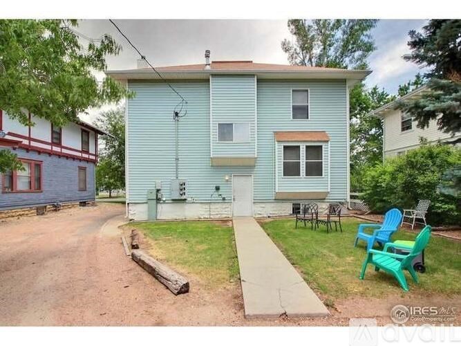 A blue house with a white door and windows, a green lawn chair, and a dirt path leading to the front door.