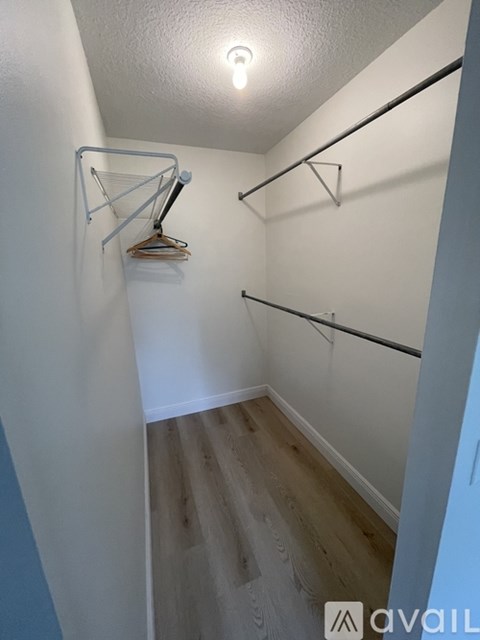 A small closet with a light on and clothes hanging up.
