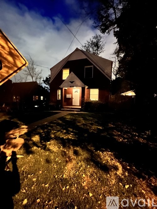 A house with a lit up front porch and a tree in front of it.