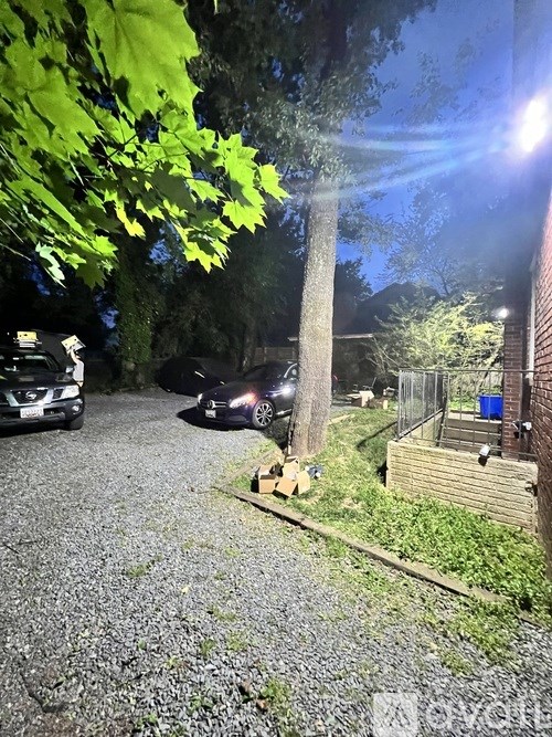 A gravel driveway leads to a dark house with a car parked in front.
