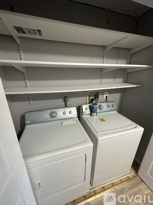 A laundry room with two washing machines and a shelf above them.