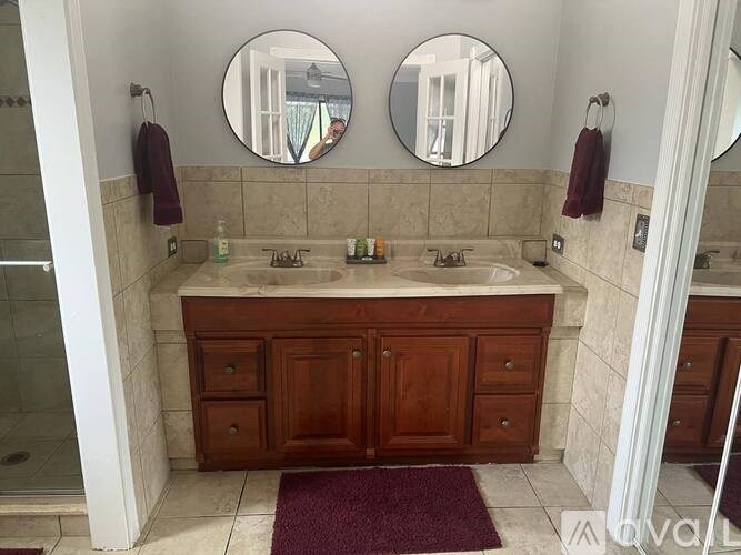 A bathroom with a maroon rug in front of a double sink vanity.
