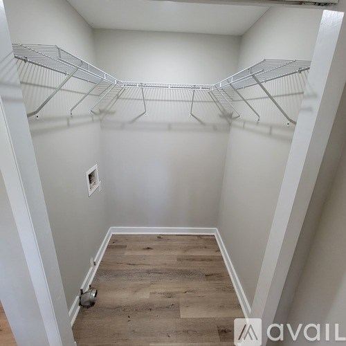 A walk in closet with white walls and wood floors.