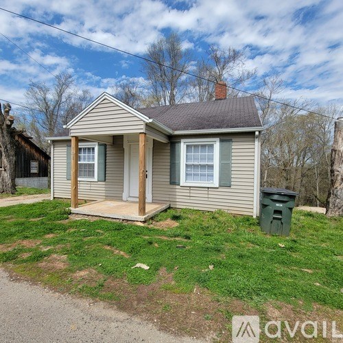 A small house with a porch and a green trash can in front.