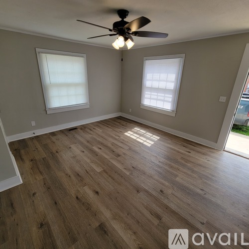 A room with wooden flooring and two windows.