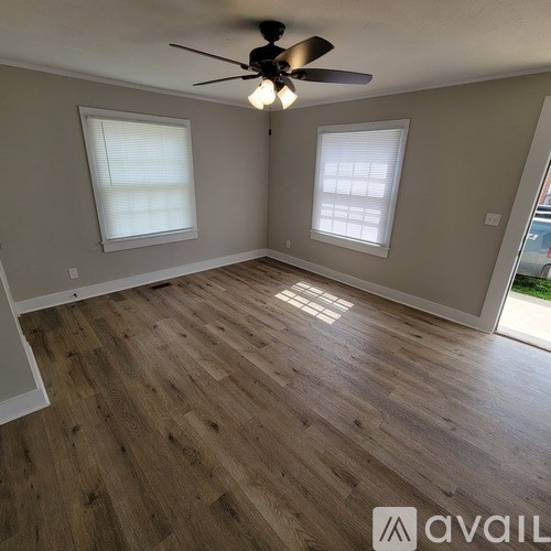 A room with wooden flooring and two windows.