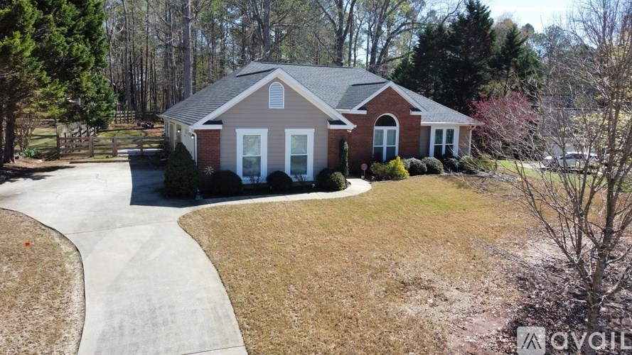 A house with a red brick exterior and white trim is surrounded by a well-manicured lawn and trees.