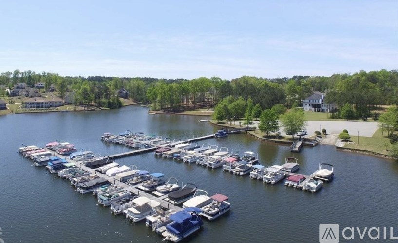 A marina with boats docked on the water and houses in the background.