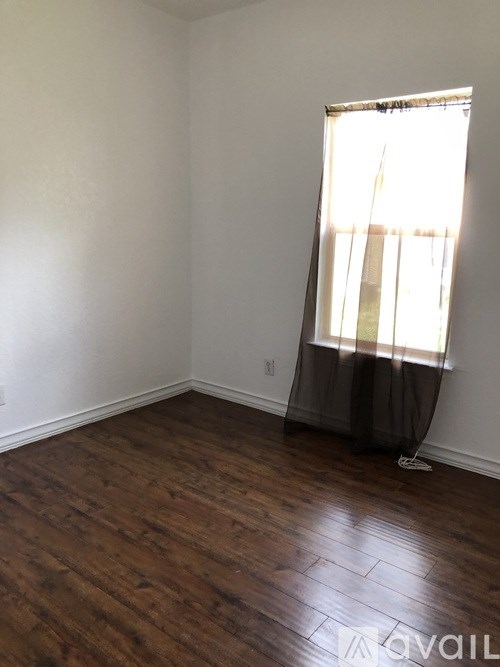 A room with wooden floors and a window with curtains.