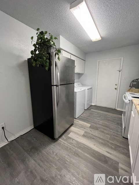 A black fridge with a plant on top in a room with a grey floor.