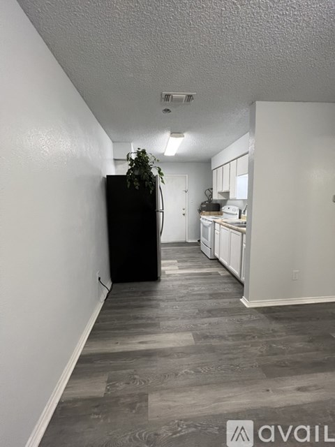 A long hallway with a black refrigerator and a kitchen area with white cabinets.