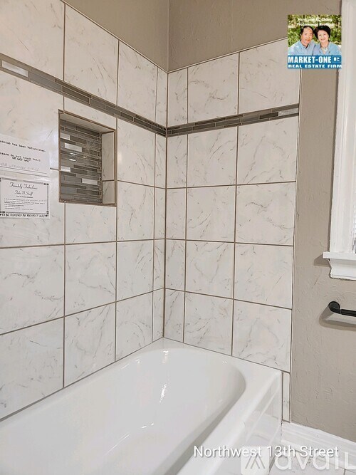 A bathroom with a white tub and a white tiled wall.