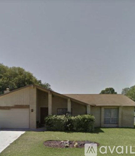 A house with a brown roof and tan walls is surrounded by a green lawn.